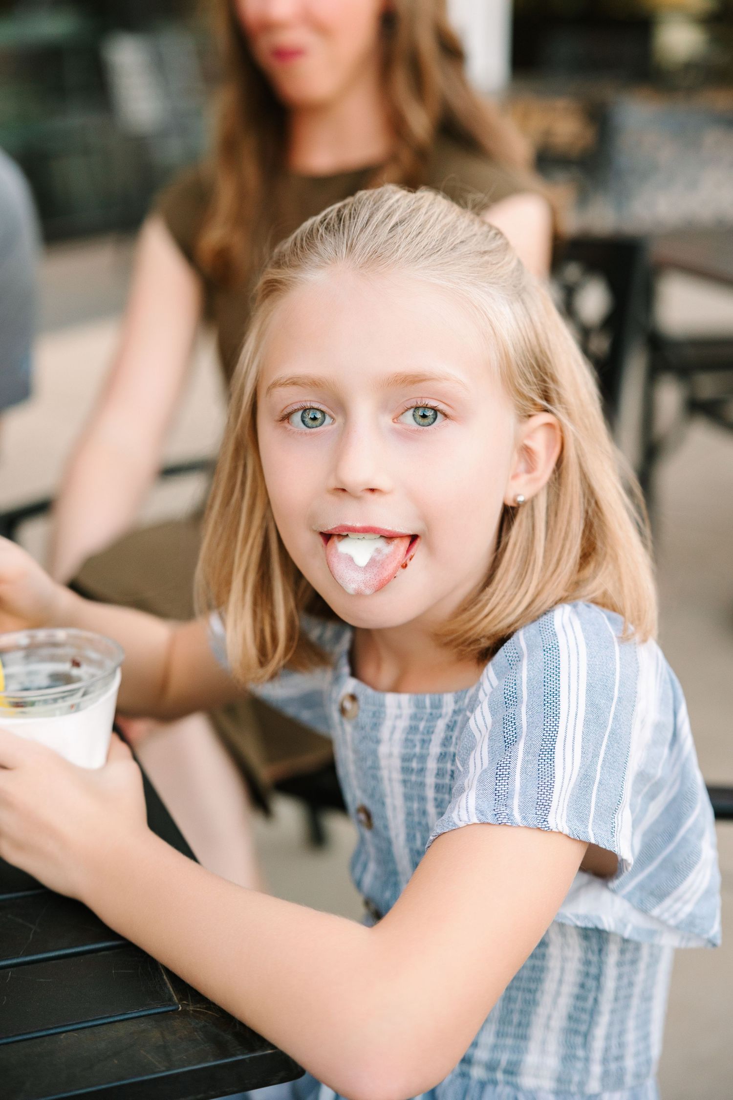 A child wearing a blue and white striped dress enjoys ice cream with whipped cream on their face.