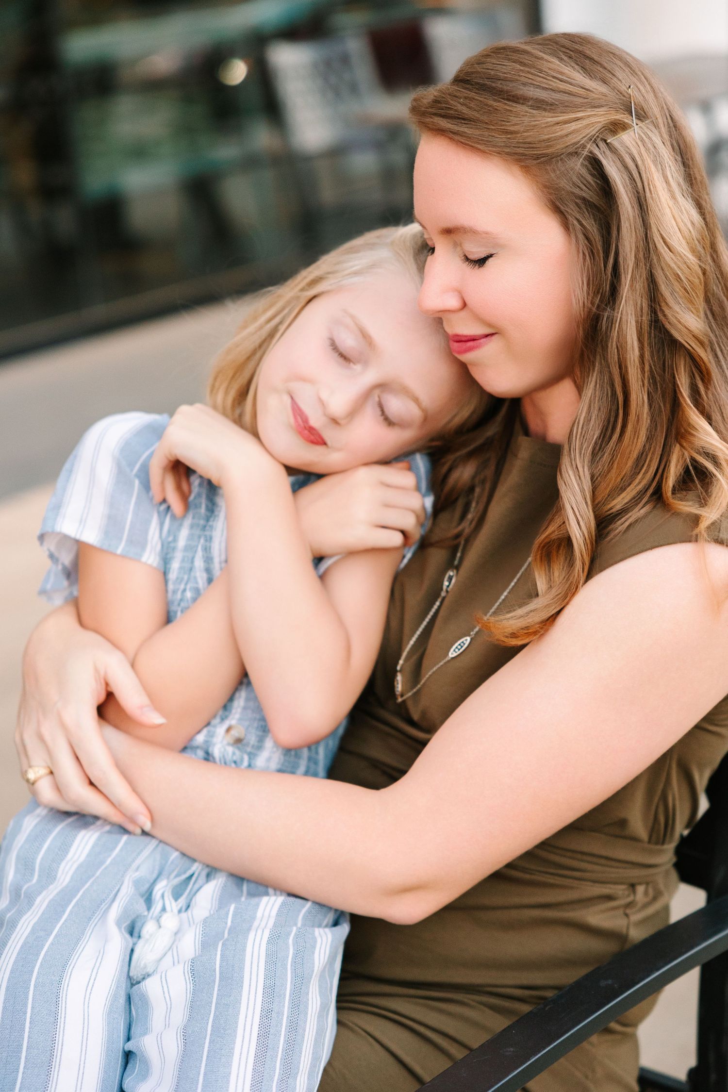 Two people share a tender embrace while seated, with one wearing a blue striped shirt and the other in olive green.