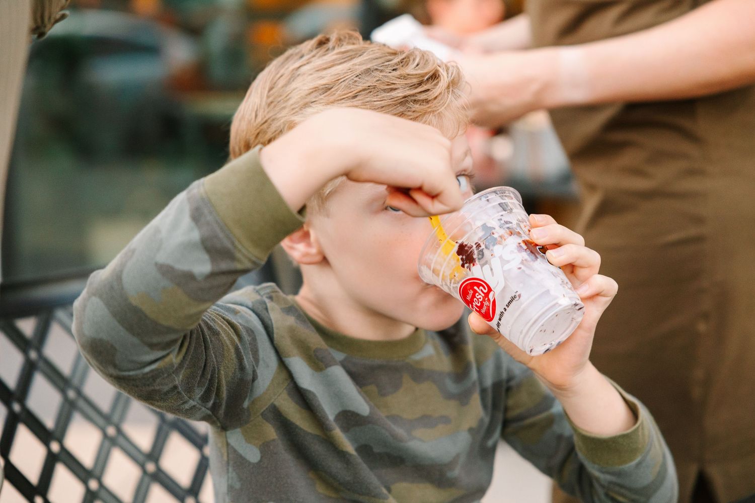 A child enjoys a frozen dessert while sitting outdoors at a cafe.