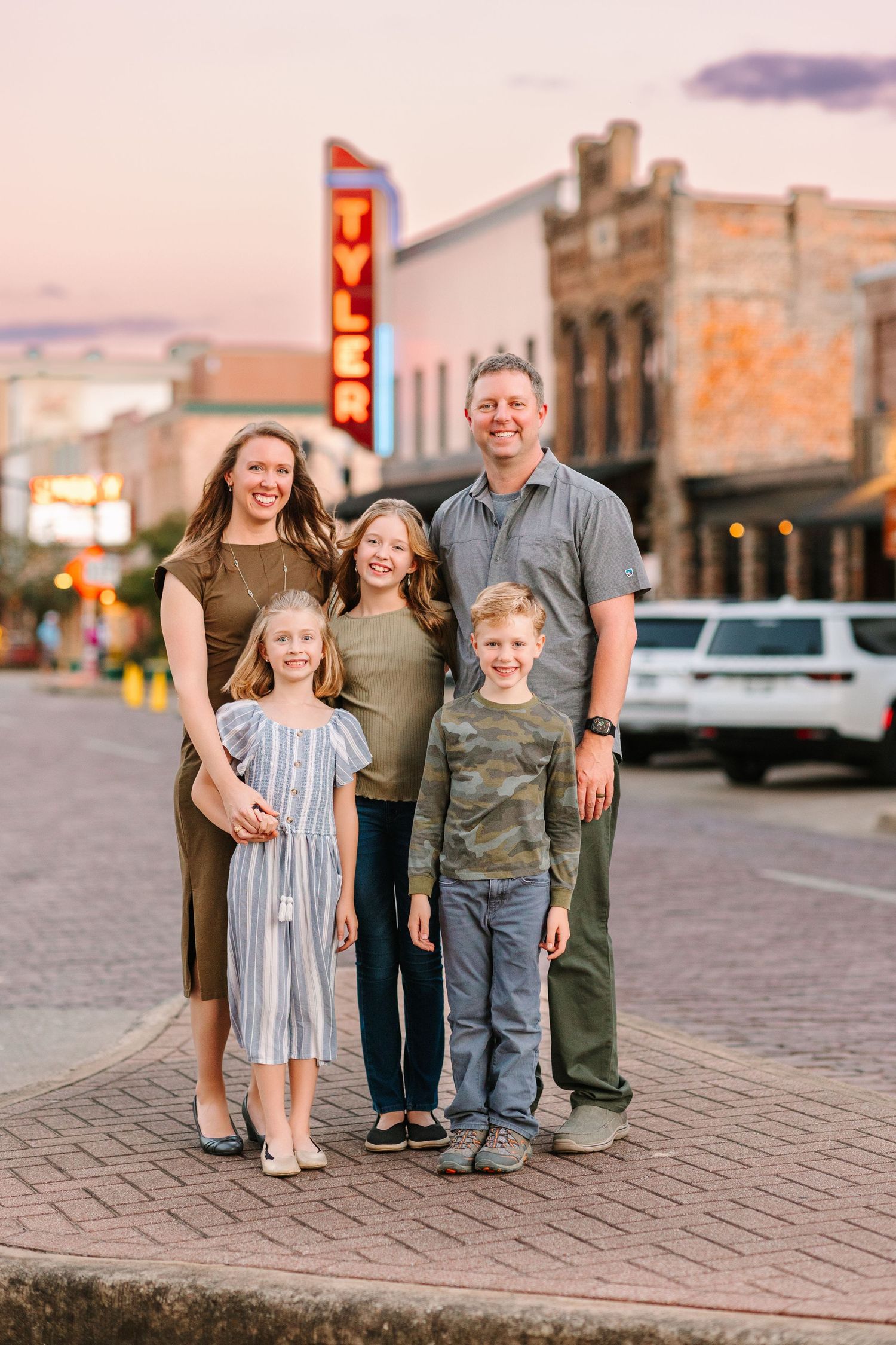 A family poses together on brick pavement in a small town setting during sunset.