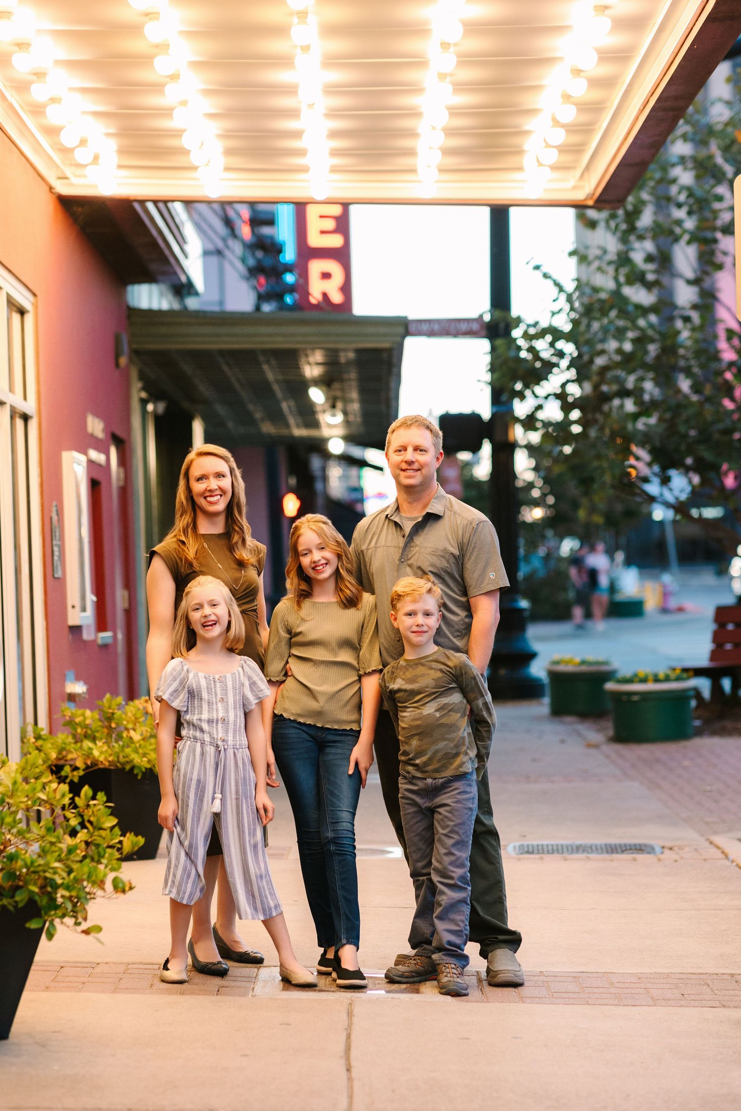 A family walks together under illuminated storefront awnings at dusk.