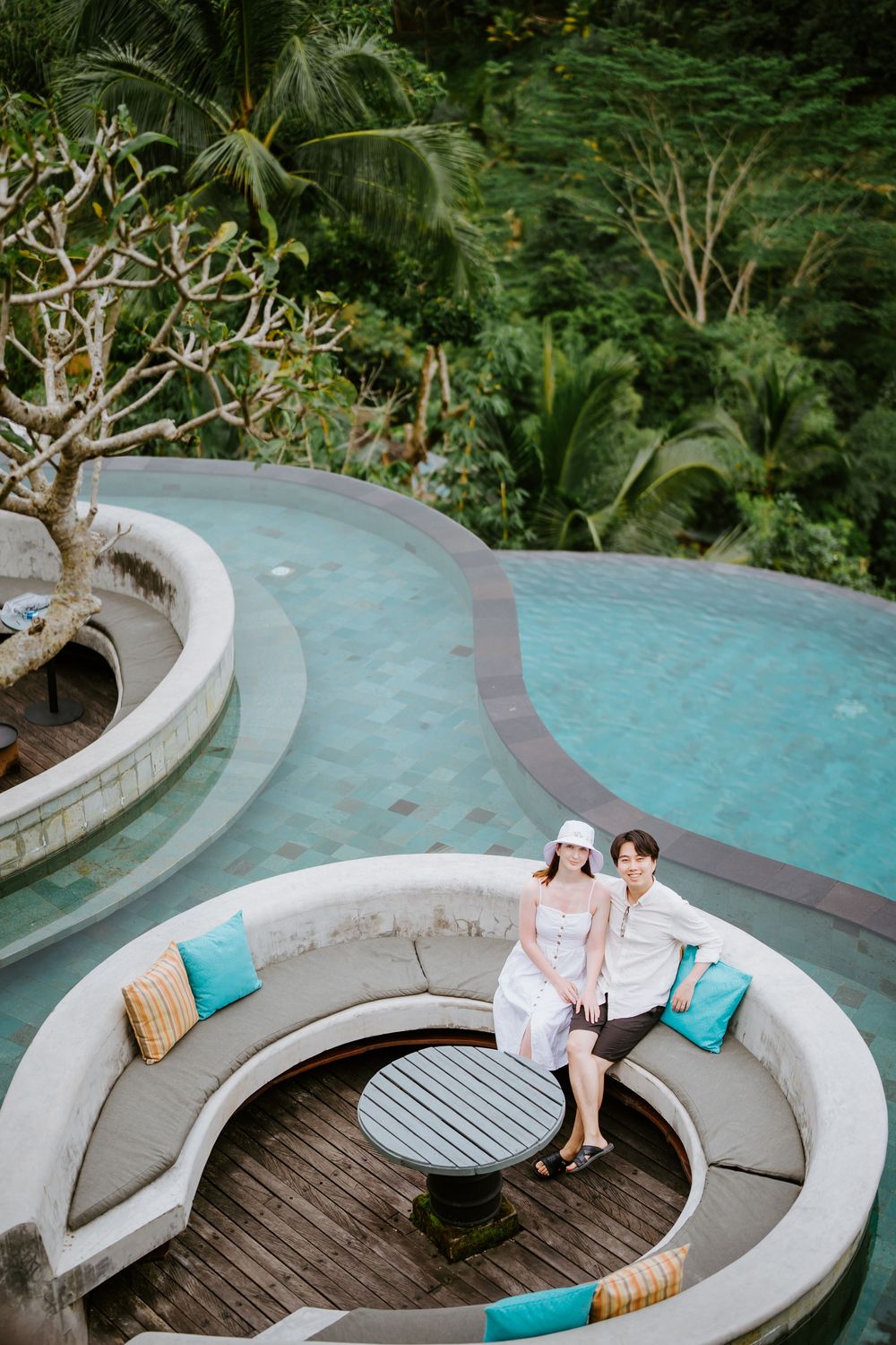 Curved poolside seating area surrounded by tropical gardens and palm trees.