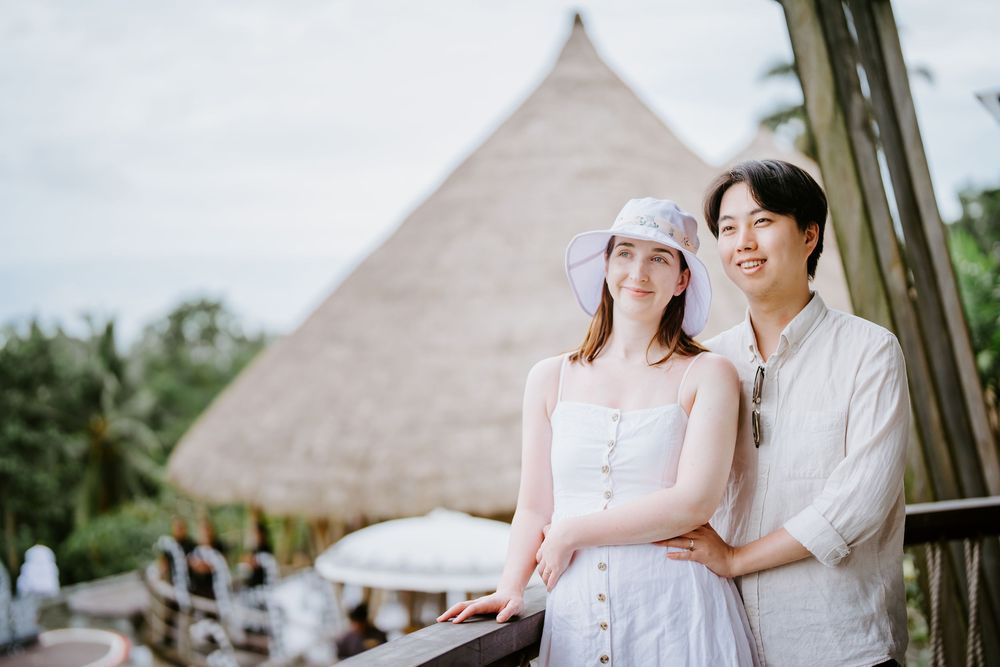 Couple enjoying a romantic moment on a balcony with a traditional thatched roof structure in the background.