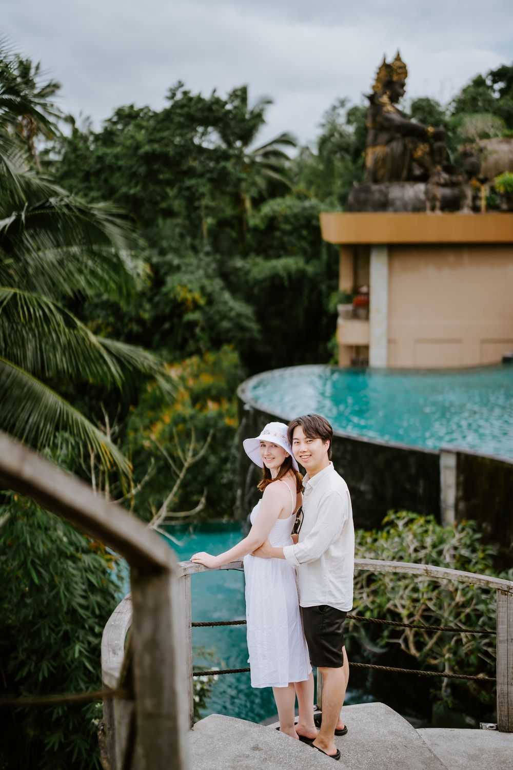 Couple standing on stone pathway overlooking infinity pool with tropical landscape views.
