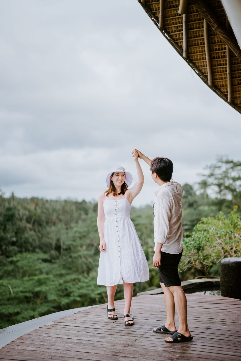 A couple in white outfits dancing together on a wooden deck overlooking tropical scenery.
