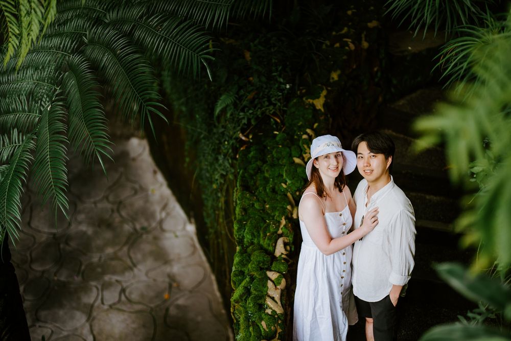 A romantic photoshoot in a lush garden setting with two people in white clothing embracing.