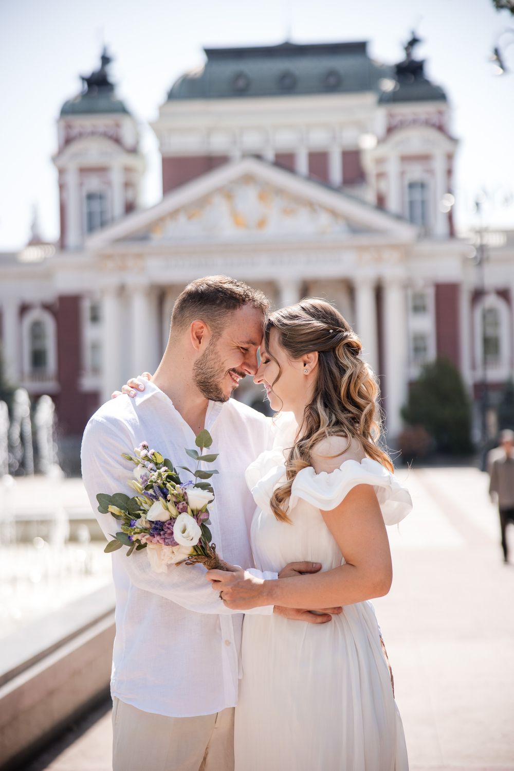 A romantic wedding couple shares an intimate moment in front of the National Theater in Sofia – bright, airy wedding atmosphere