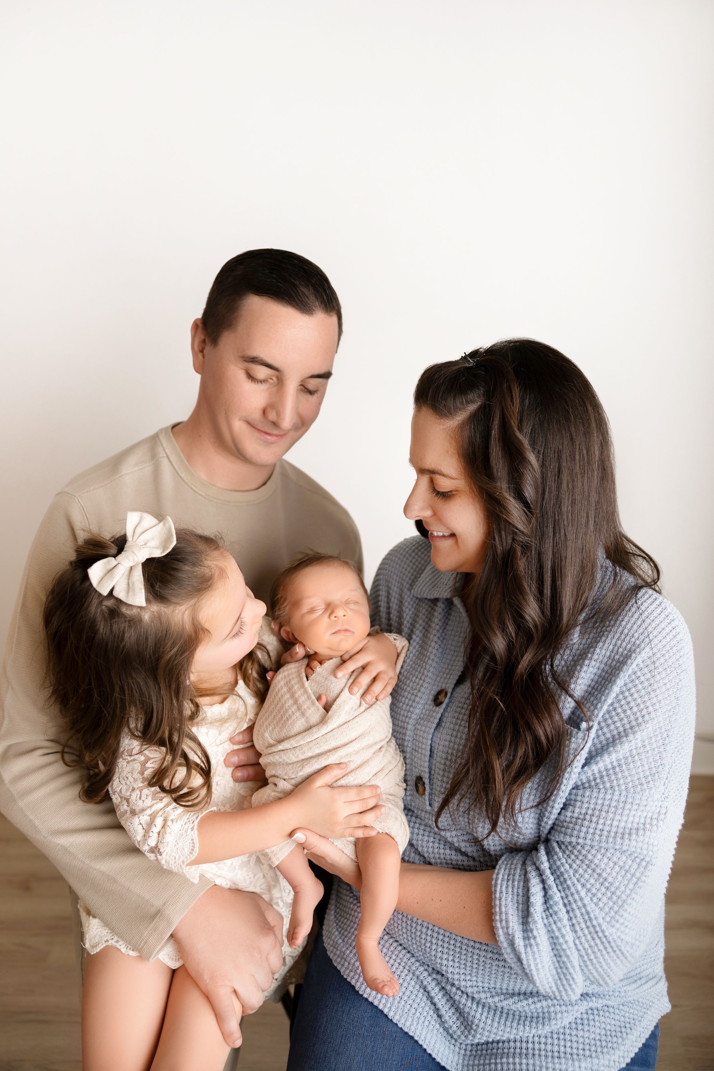 A loving family shares tender moments together in a series of warm studio portraits with neutral backgrounds.