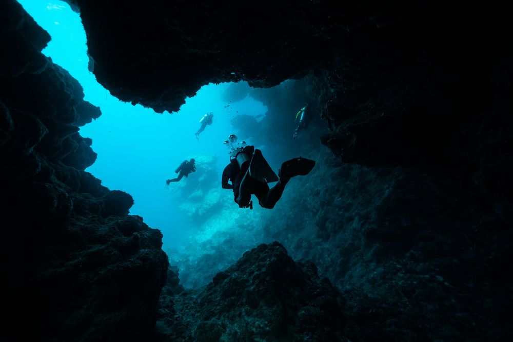 A scuba diver silhouetted against bright blue water while exploring an underwater cave formation.