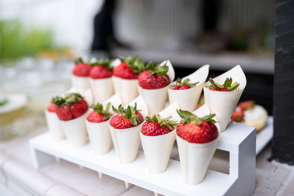 Fresh strawberries and whipped cream served in individual white ceramic cups on a serving tray.