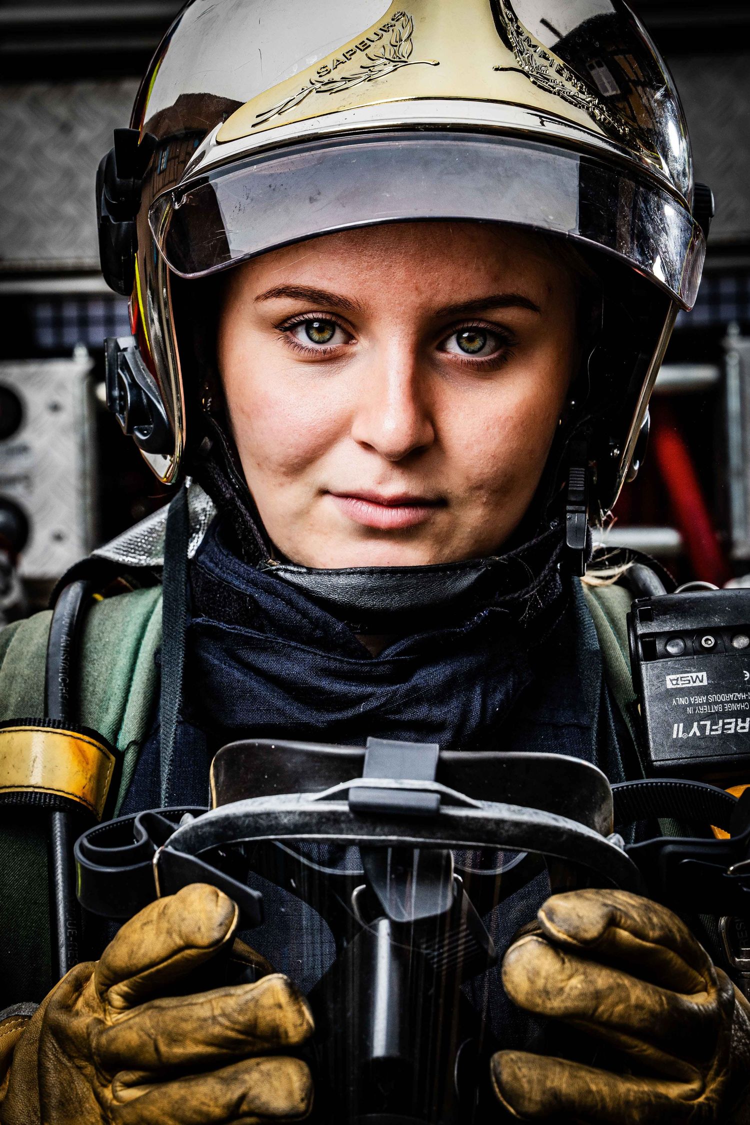 Close-up portrait of female firefighter in helmet and gear holding radio equipment.