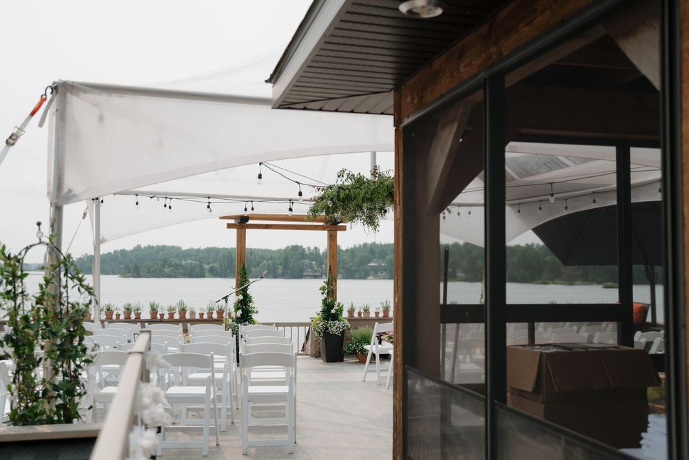Covered outdoor wedding venue with white chairs set up overlooking a serene lake.