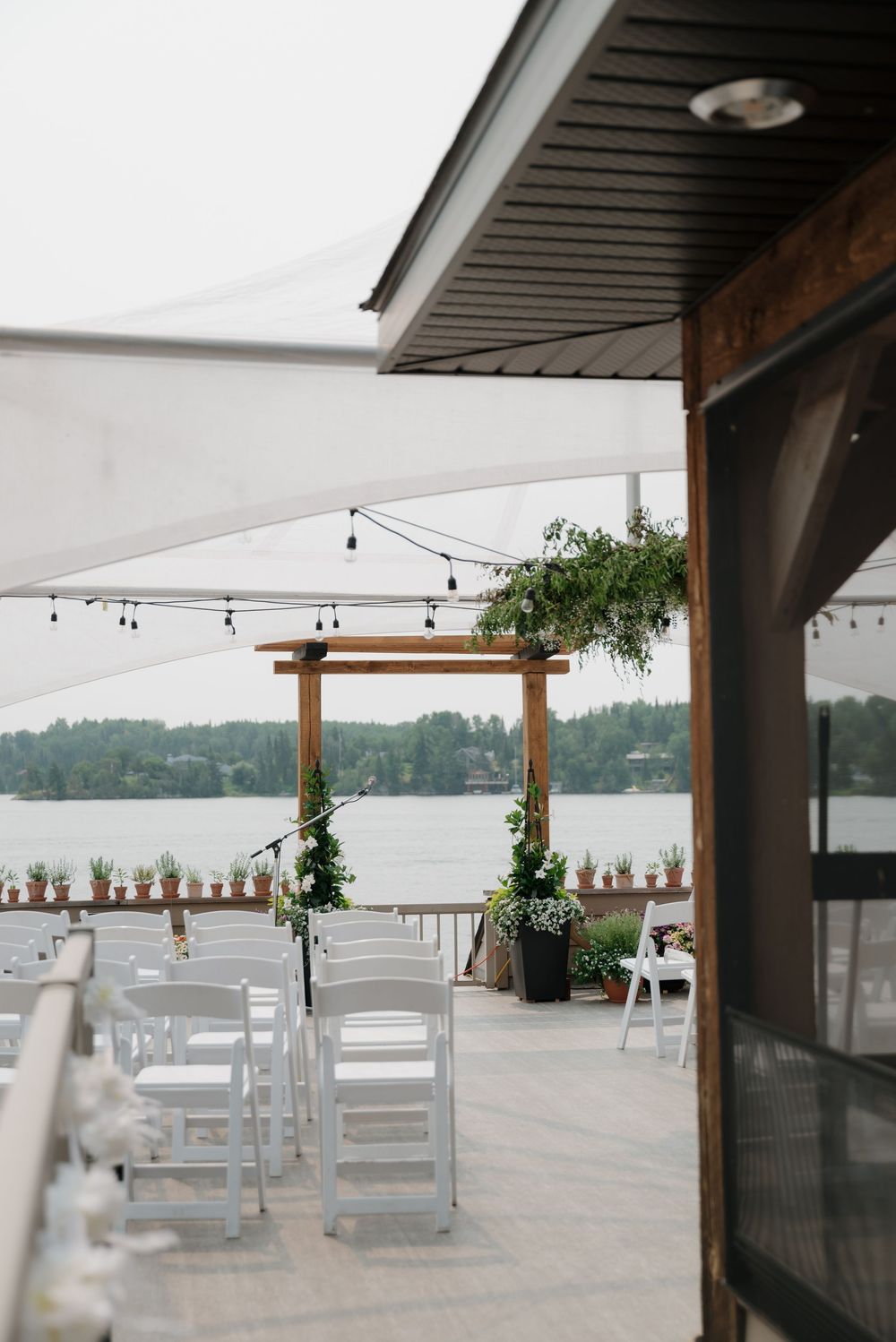 Lakeside wedding ceremony setup with white chairs and wooden arch decorated with greenery.