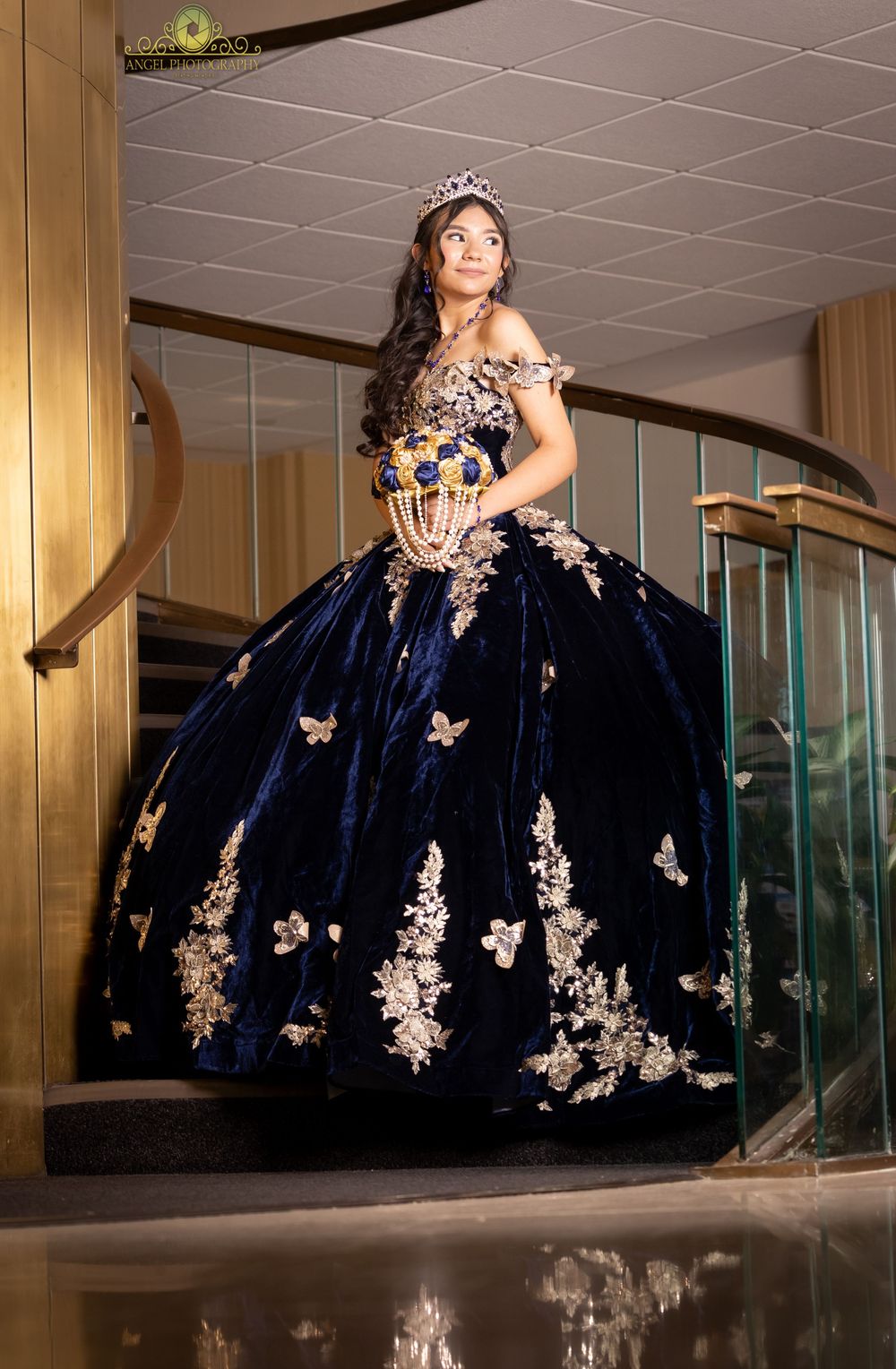 Elegant navy blue ballgown with gold lace appliques and butterflies photographed in a luxurious venue hallway.