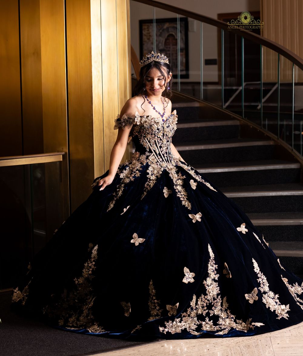 A formal black ball gown with intricate gold lace appliques and a dramatic full skirt photographed in a hallway.
