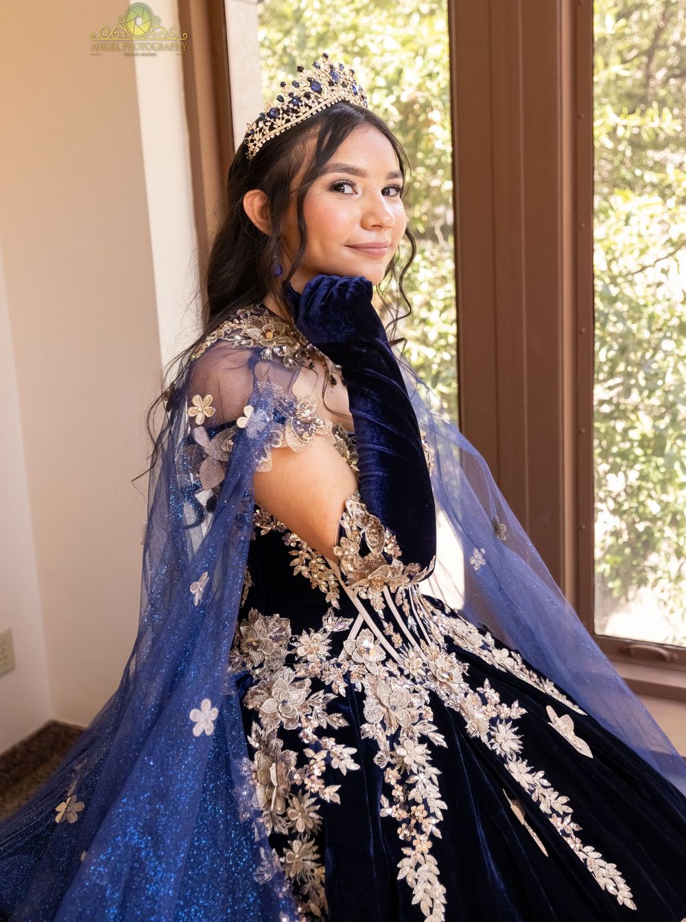 Elegant royal blue and silver ball gown with floral lace appliques, sheer cape and sparkling tiara for formal occasion.