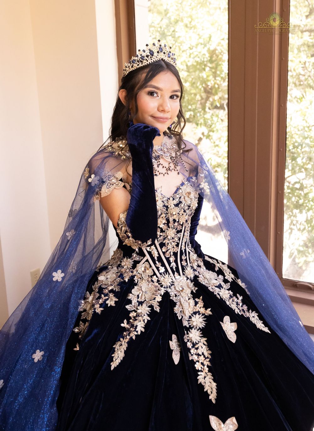 Elegant navy blue and white ball gown with intricate floral lace appliques and flowing cape detail photographed in natural light.