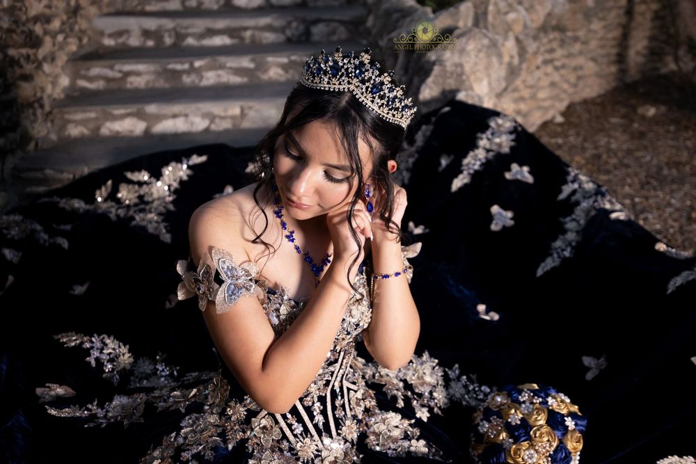 A pageant contestant in a silver tiara and elegant dress poses against a textured stone background.