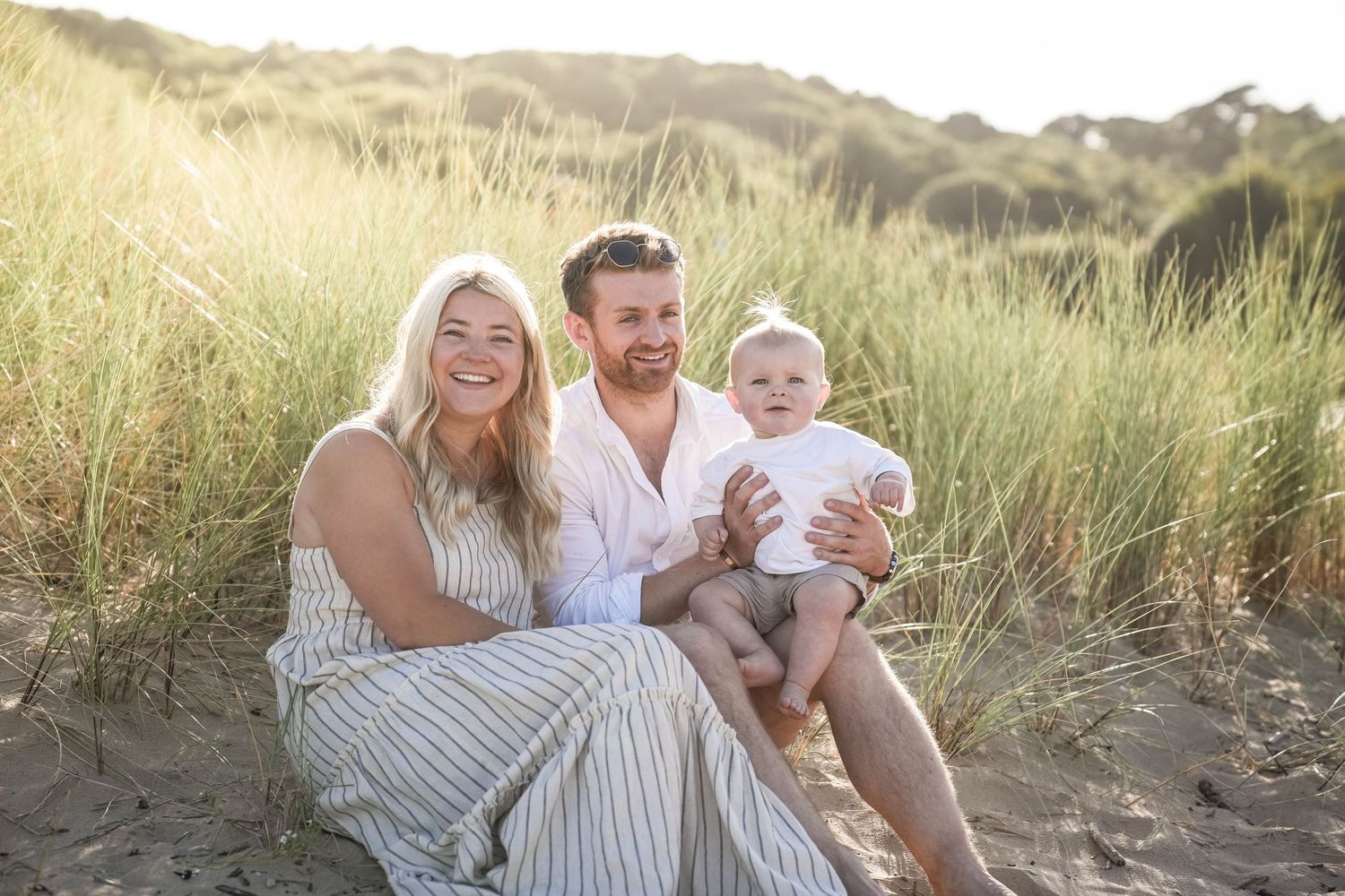 A group sits together on a grassy hillside during golden hour wearing coordinated white and neutral colored outfits.