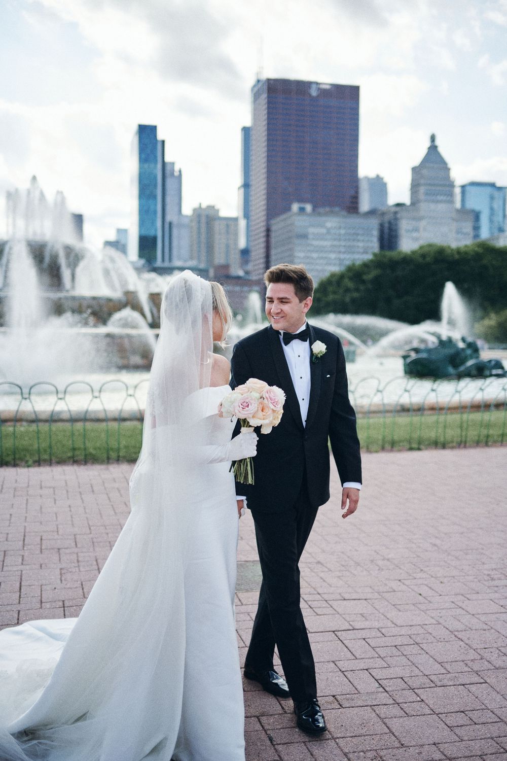 Wedding couple poses near Buckingham Fountain in Chicago with dramatic city skyline in background.