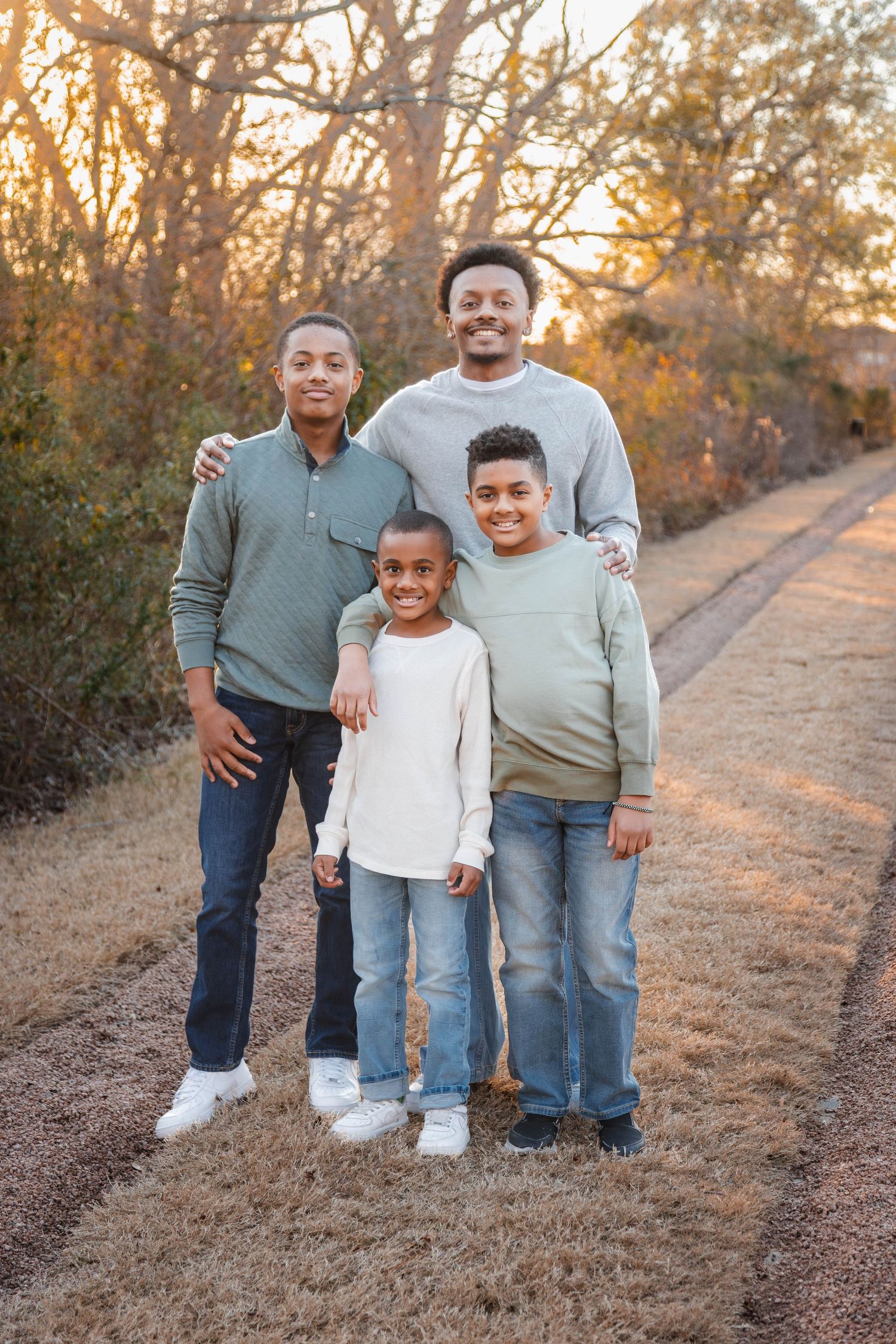 Three siblings stand together on a dirt path during golden hour in coordinating neutral outfits.