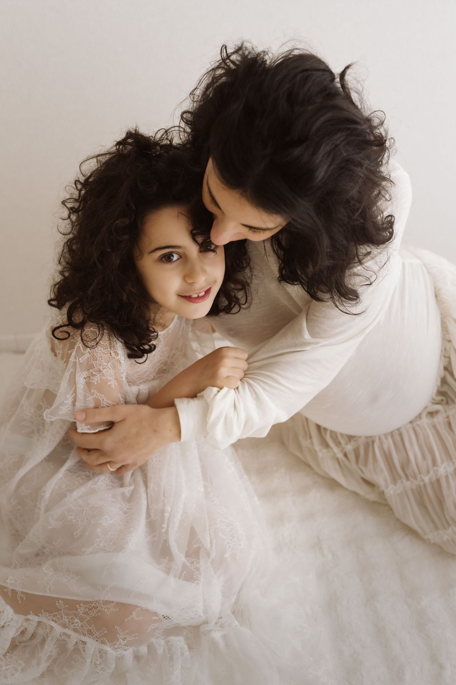 A romantic couple in white outfits sharing an intimate moment with their curly dark hair framing the tender scene.