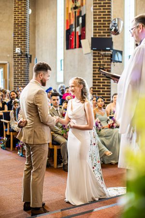 Bride and groom holding hands at the church altar during their wedding ceremony with guests watching.