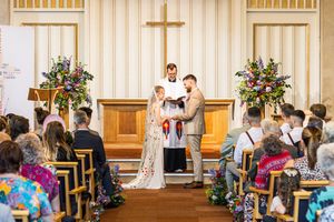 Bride and groom at the altar during wedding ceremony with colorful floral arrangements and seated guests.
