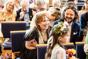Wedding guests laugh and chat warmly during the ceremony, with a flower girl in foreground.