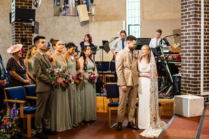 Bride and groom stand at the altar during wedding ceremony with bridesmaids holding colorful bouquets.