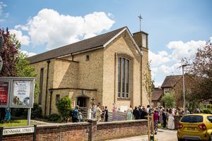 Wedding guests gather outside a brick church on Denmark Street under a bright blue sky.