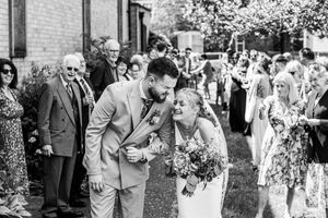 Black and white photo of laughing bride and groom sharing joyful moment during confetti walk at wedding.