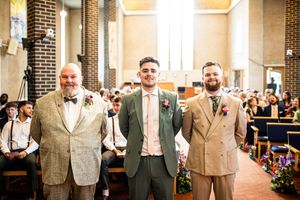 Groom standing at the church altar with two groomsmen, smiling at guests before the ceremony.