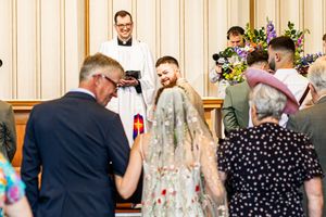 Bride and groom laughing during wedding ceremony while officiant reads from a book at the altar.
