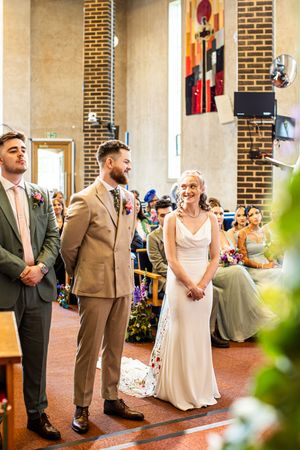 Bride and groom exchanging vows at church altar, smiling joyfully with wedding guests seated behind them.