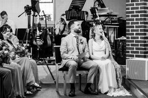 Black and white photo of bride and groom seated together during wedding ceremony with live band behind them.