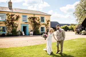 Bride and groom strolling hand in hand on a gravel path outside a charming yellow country house.