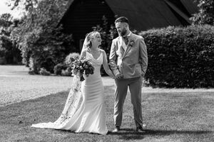 Black and white photo of bride and groom walking hand in hand across a sunny lawn.