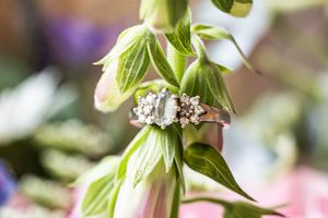 Delicate diamond and gold cluster engagement ring displayed on green foxglove flower petals outdoors.
