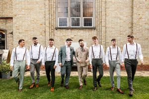 Groom and groomsmen in suspenders and grey trousers walking together outside a brick building.