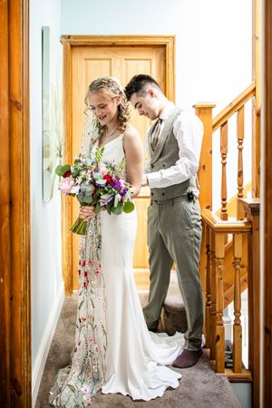 Bride and groom sharing a first look moment on a staircase, bride holding a colorful floral bouquet.