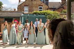 Bridesmaids in sage green dresses standing in a sunny outdoor garden waiting for the bride.