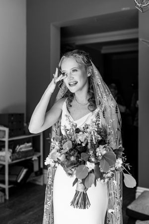 Black and white portrait of an emotional bride in a floral veil holding a bouquet and wiping a tear.