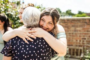 A smiling woman hugging an older woman with grey hair at an outdoor wedding celebration.