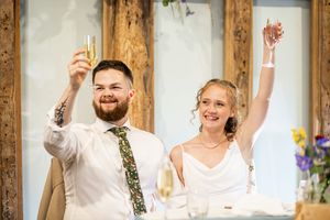 Bride and groom raising champagne glasses in a joyful wedding toast inside a rustic barn venue.