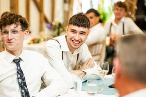 Young male wedding guest smiling warmly at the reception table in a rustic barn setting.
