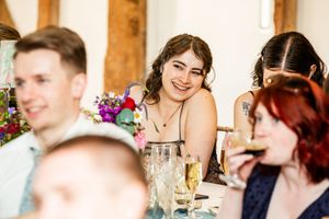 Smiling female wedding guest leaning on table surrounded by colorful floral centerpieces at reception.