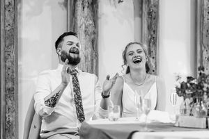Black and white photo of bride and groom laughing heartily together at their wedding reception.