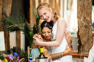 Two brides share a joyful embrace at their wedding reception, one in white dress hugging the other warmly.