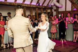 Bride and groom share their first dance at a rustic barn wedding reception with guests watching and applauding.